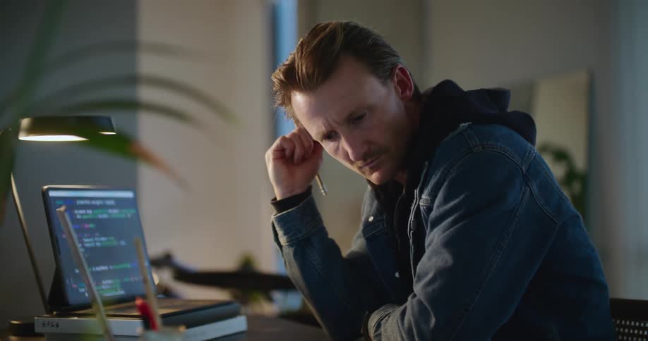 Man thinks while sitting at desk with computers before typing
