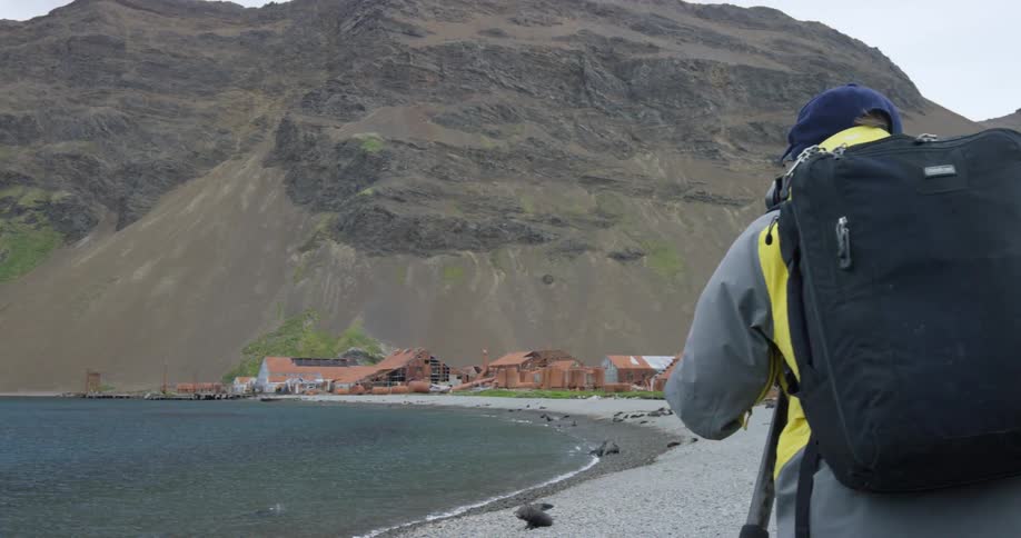 A photographer with a backpack takes pictures of a village on a shore