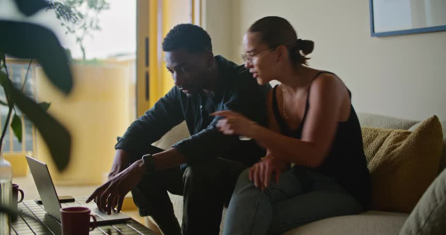 A man and woman sit on the couch together looking at a laptop