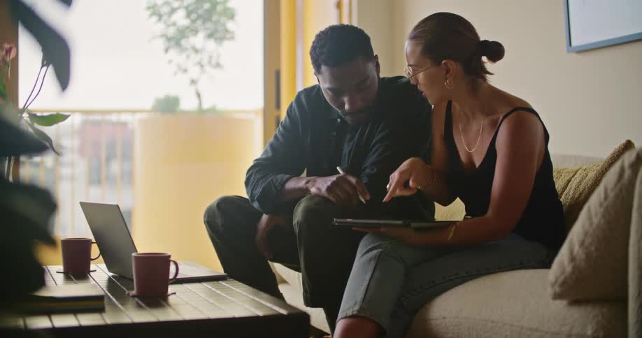 A man and woman look at a tablet together while sitting on the couch