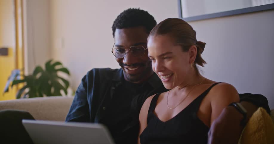 A couple sit on the couch looking at a laptop