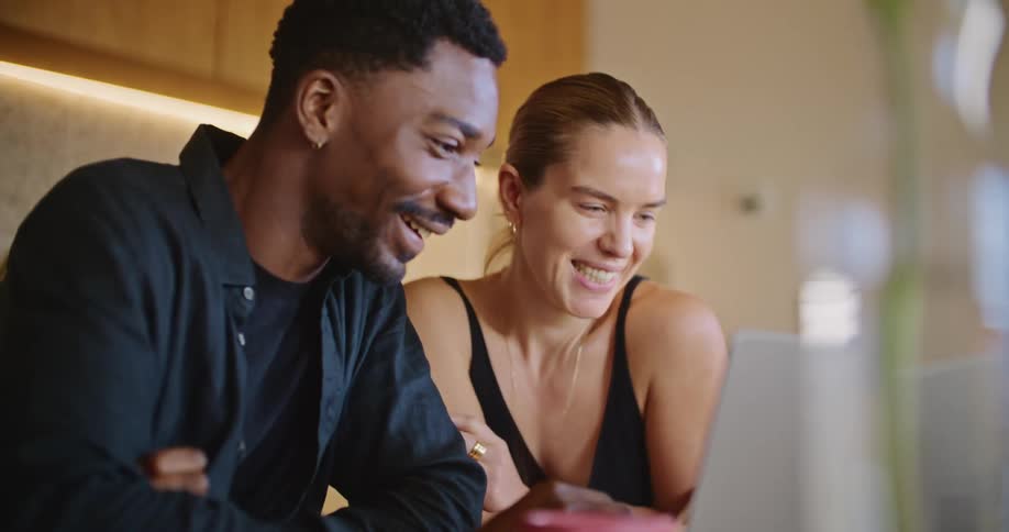 A man and woman laugh while looking at a laptop together