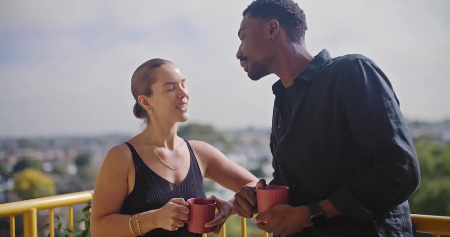 A couple kiss while drinking coffee on their balcony