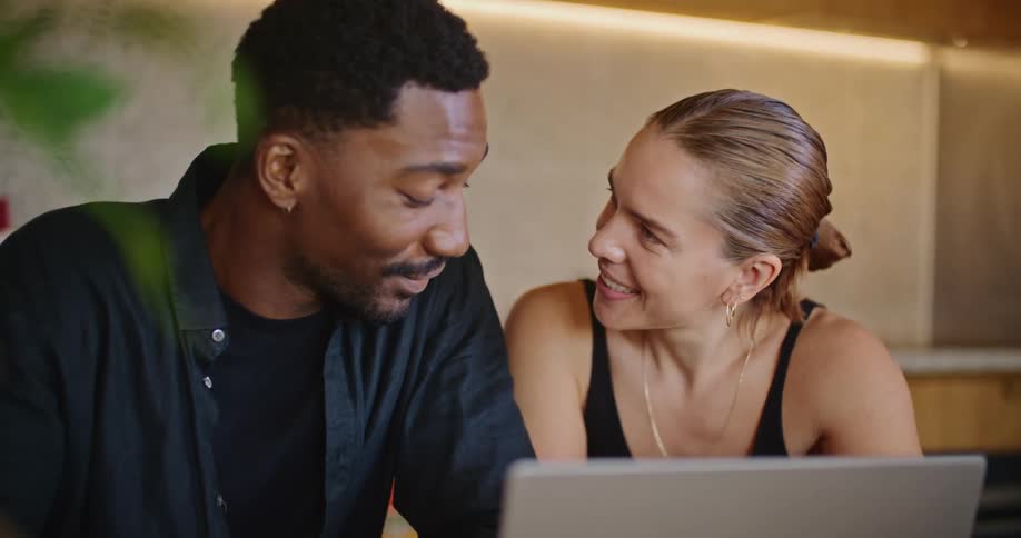 A man and woman sit in front of a laptop and talk and laugh with one another