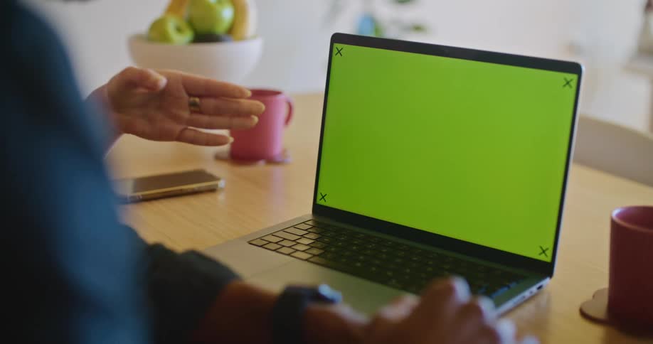 Woman puts down mug and gestures at laptop screen while holding discussion with coworker