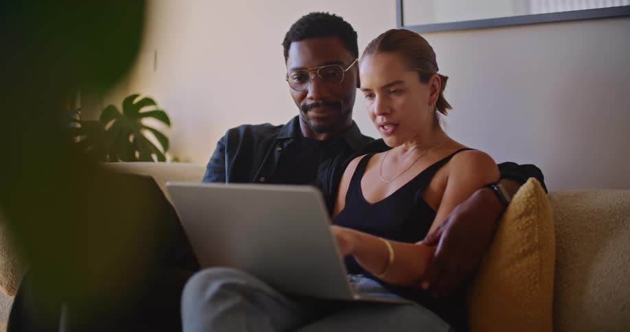 A man sits with his arm around his partner while they look at a laptop