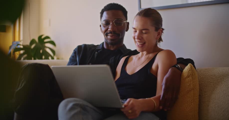A man and woman laugh while looking at a laptop