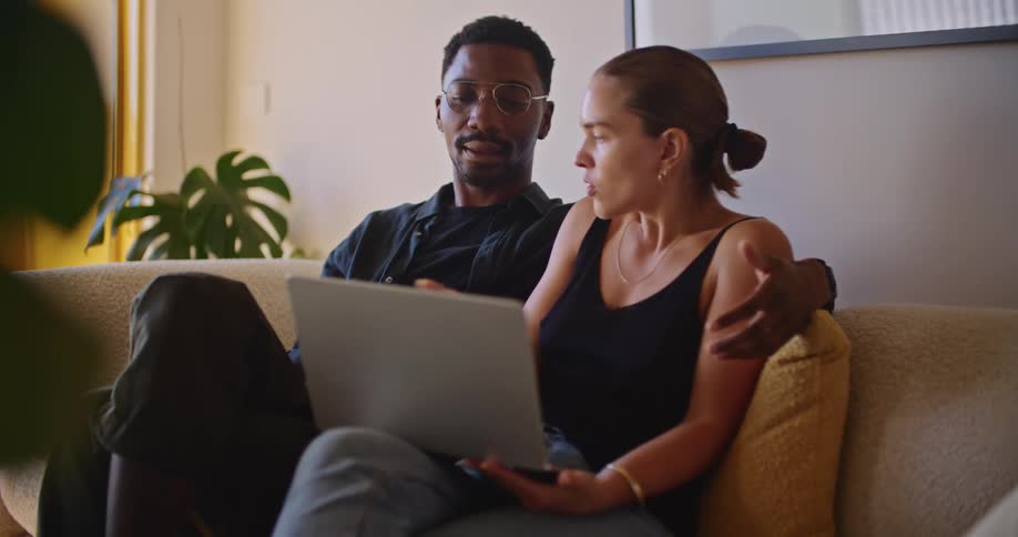 A man and woman sitting on a couch together talking while the woman has a laptop on her lap