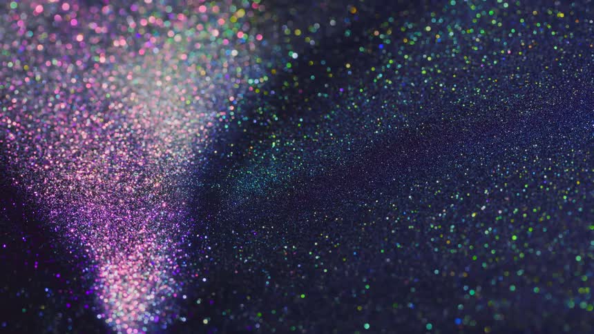 Colored glitter sparkles in the darkness as it moves away from a sparkling pink area
