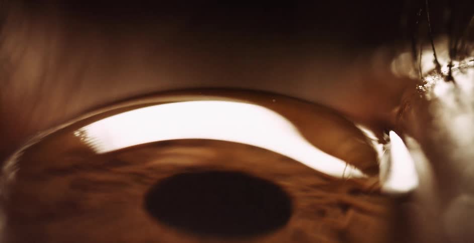 An extreme closeup shows the surface of a persons eyeball as they blink