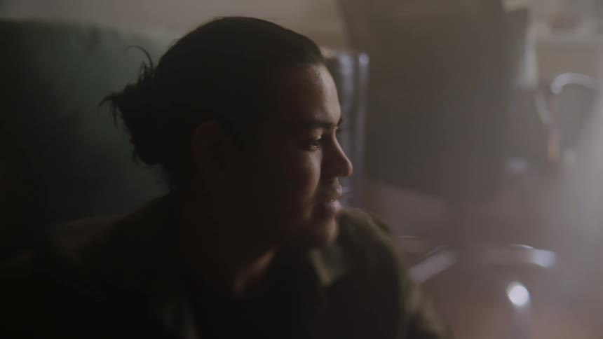 A mans face as he sits on the floor looking front of him talking to someone
