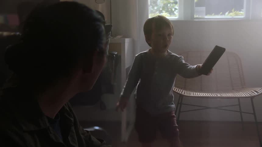 A young boy grabbing a remote off a counter and handing it to a person next to a woman sitting on the floor