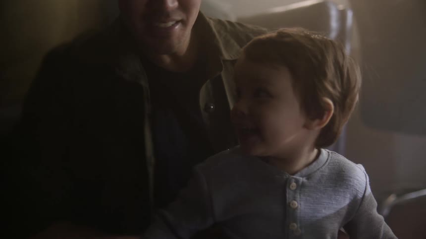A man sits while holding a young boy and wiggles a little bit