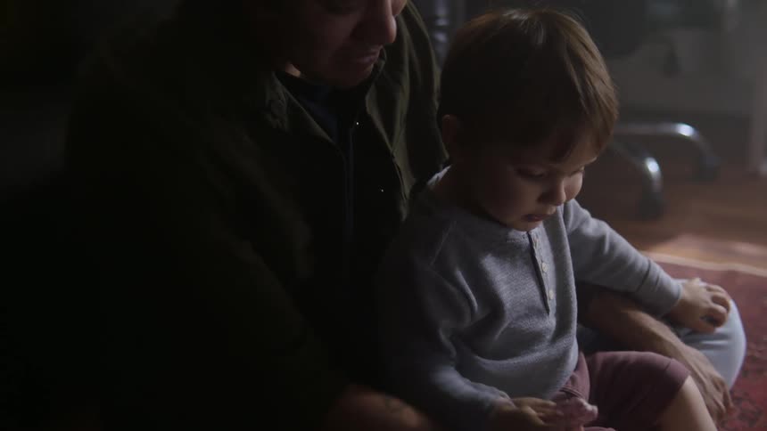Toddler son sits on fathers lap in room