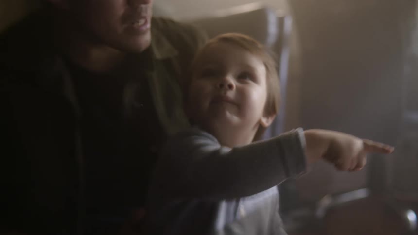 A little boy on a mans lap looking around pointing and talking