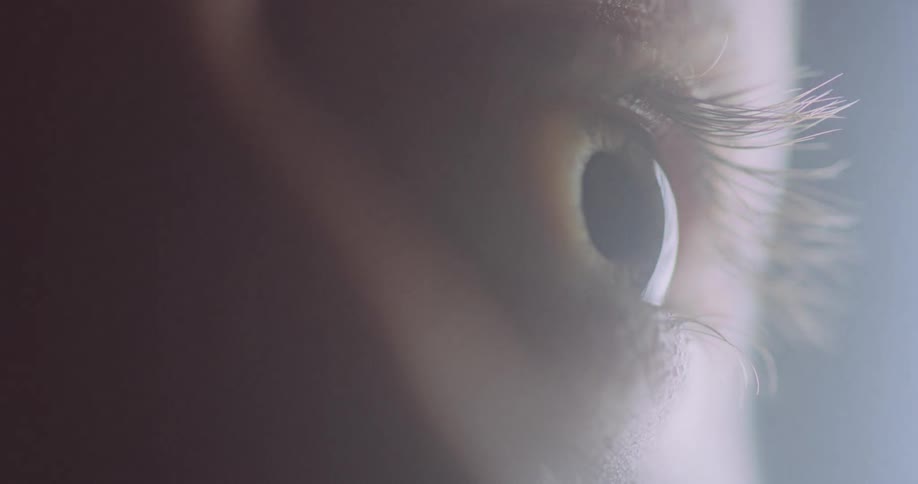 A closeup of a a human eye is seen as a bright light shines nearby
