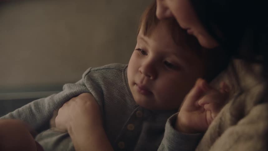 A close up of a toddler boy sitting in his mothers arms as she rocks side to side