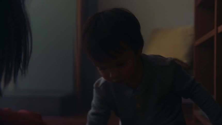 A happy young child is drinking from a cup and playing with his mom on the floor of a room in the house