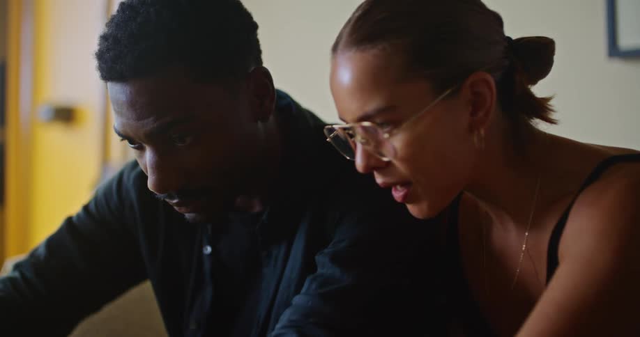 A laptop sitting on a tile table top and a man and woman looking at it and having a conversation