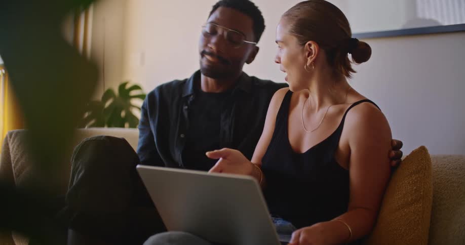 Man and woman sitting on a couch in their living room the woman with a laptop on her lap they are looking at and discussing something