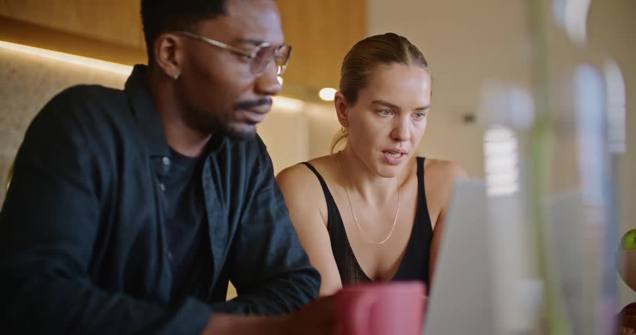 A man and a woman are sitting at a table talking as they look at a laptop computer