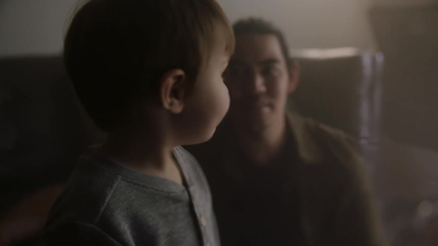 A man sits on the floor of his living room with his toddler