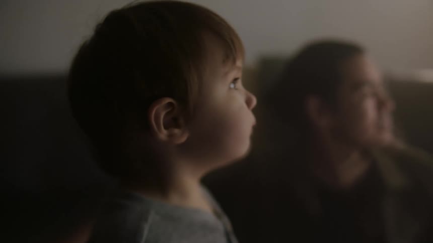 Close up of the face of a baby sitting with his father on a couch at home