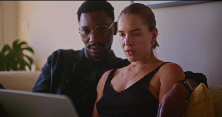 A man and woman sitting on a couch looking at a laptop while they talk