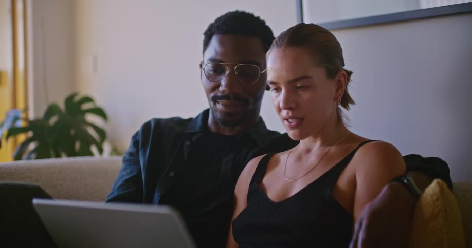 Close up of a young couple comfortably sitting together in the couch looking at a laptop while talking
