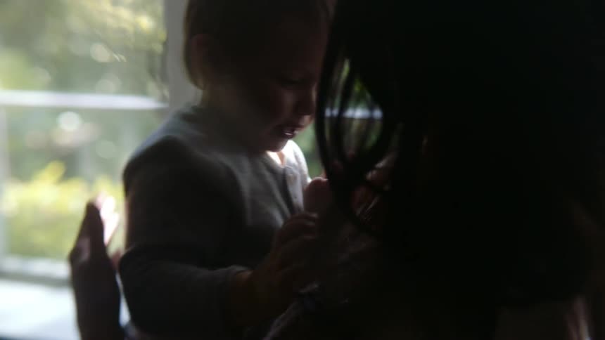 Silhouette of the face of a mother playfully kissing and cuddling her son at home near a window