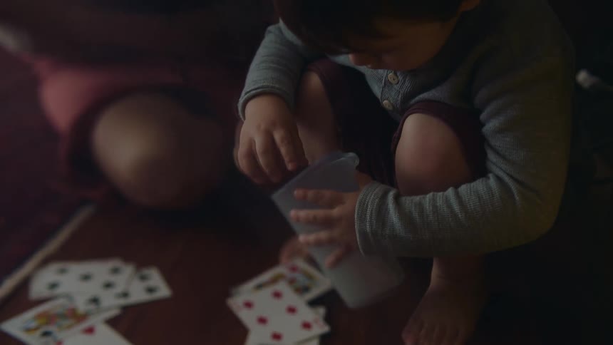 A mother and her son pick up cards from a deck off the floor and put them in a plastic cup