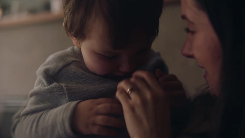 Mother with dark hair and rings holds toddler son playing with