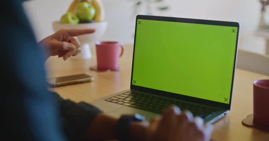 Two people are sitting at a table in front of a laptop computer with a green screen