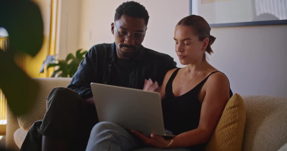 A woman is sitting on the couch with a laptop computer and talking to the man sitting next to her