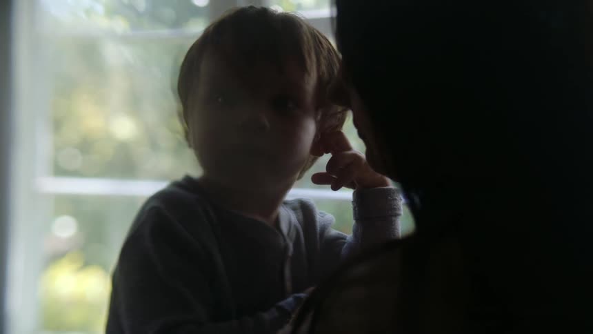 Silhouette of the face of a mother playfully kissing and cuddling her son at home near a window