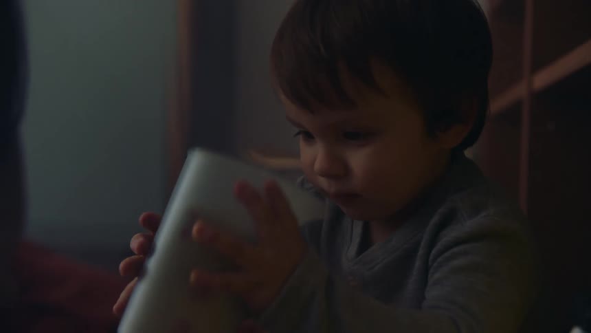 Small boy sitting on the floor of a room at home shakes a container with toys