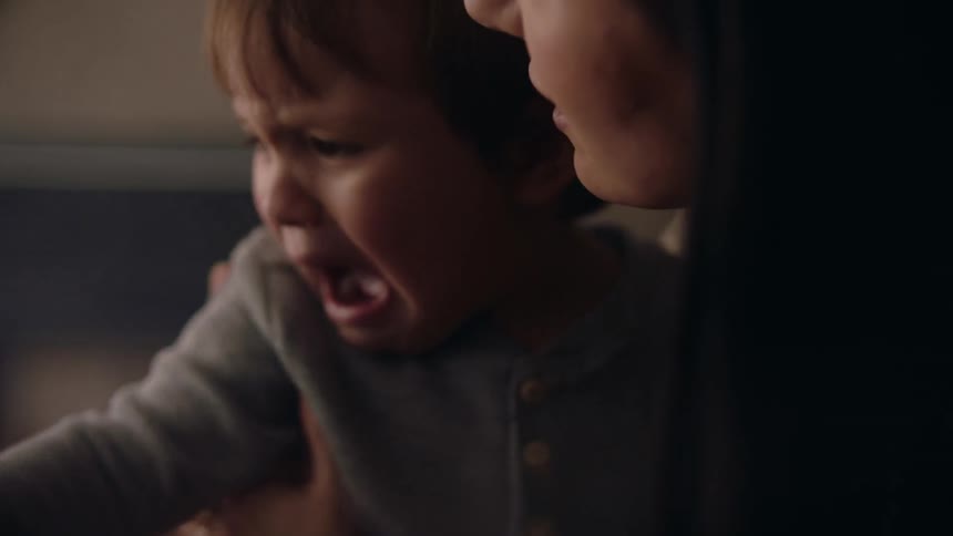 Close up of a baby crying on the arms of his mother at home