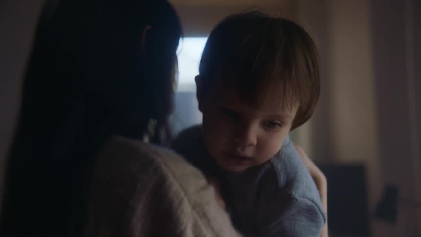 A mother is rocking her toddler son in her arms as the toddler babbles and smiles