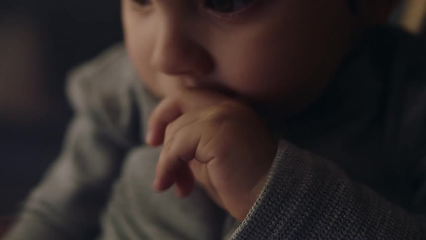 A small infant holds it hand to its mouth while looking at something in front of it