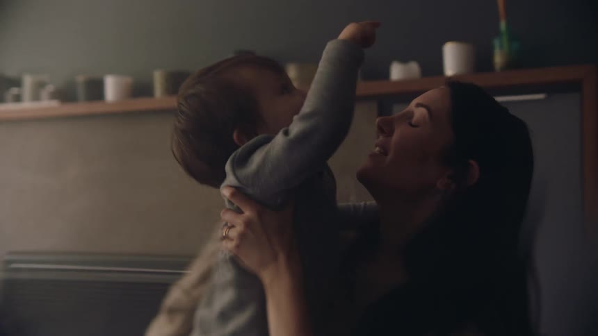 Mother with long dark hair holds toddler son wearing gray shirt and crimson pants