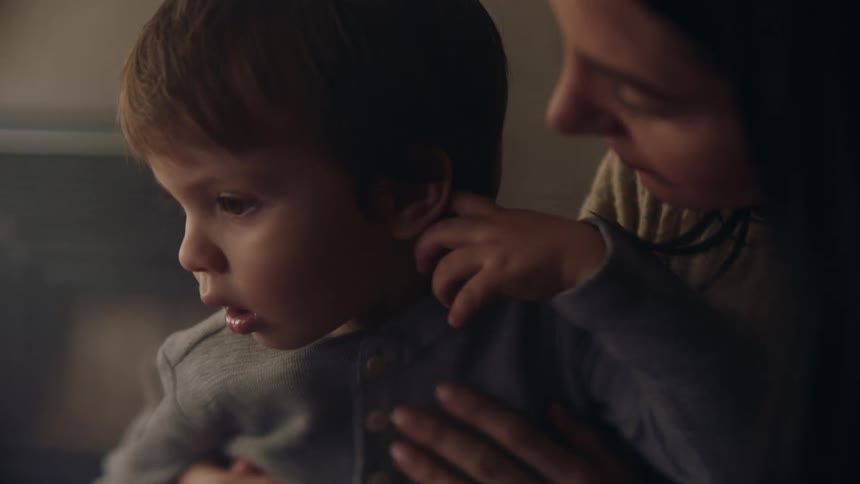 A mother holds her toddler son on her lap while kissing and playing with his face