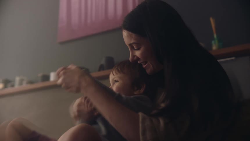 A mother holds her son in her lap and plays with him smiling and laughing