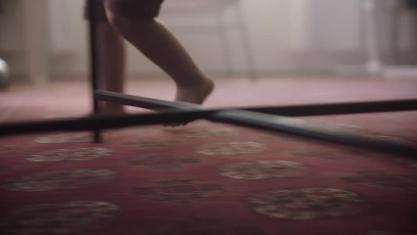 A toddler uses their legs and feet to navigate around a table across a carpeted room
