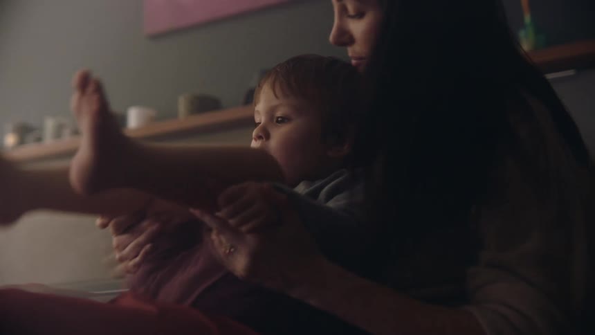 Mother cuddles with her son at home playfully tickling him