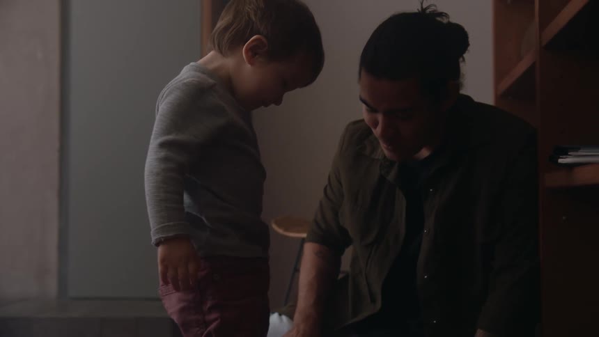 A child walks over to his father and mother sitting on the floor and picks up the cards and drops them all over