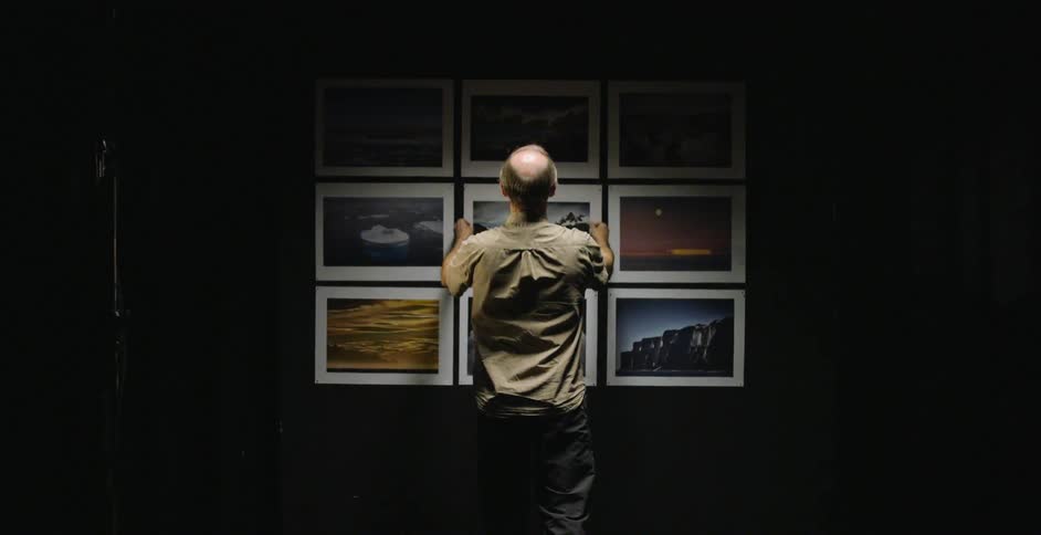A man hangs a photograph in the middle of a group of photographs