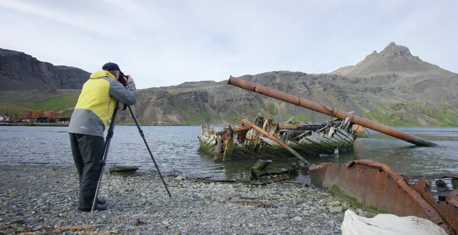 A man is photographing a crashed ship near the shore