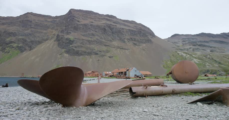 Abandoned and rusty boat parts sit on a rocky beach