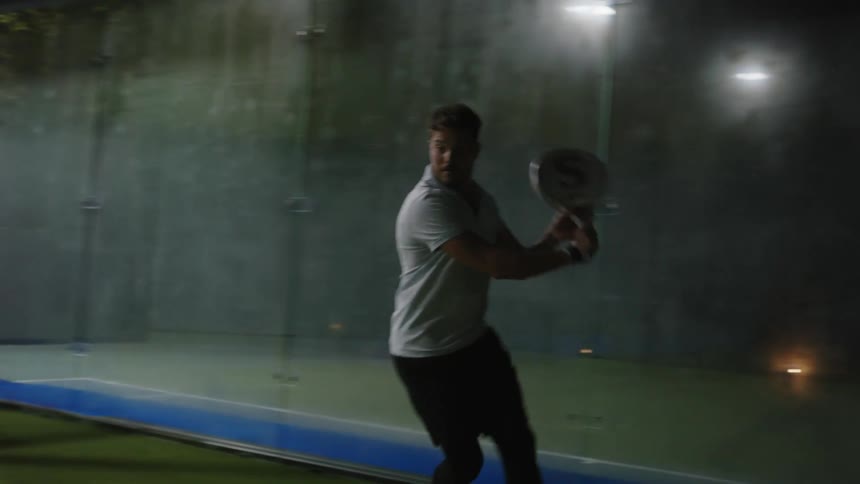 A young man is playing tennis outside at night time