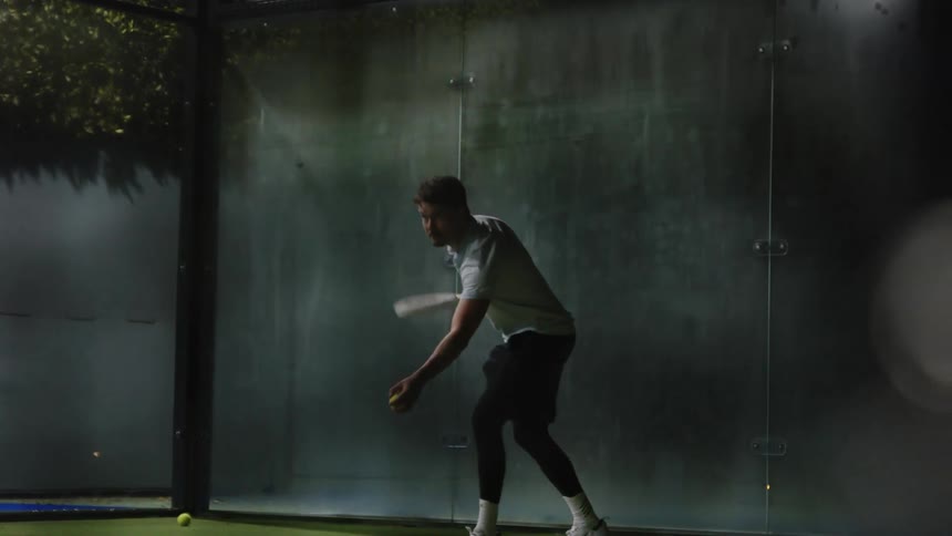 A young man serves a tennis ball on a court at night